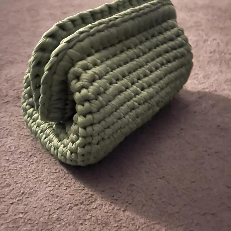 A sage green T-shirt yarn clutch on a carpet.