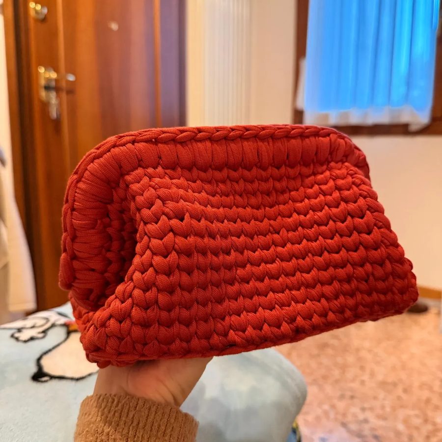 A rust red T-shirt yarn clutch held in one hand.